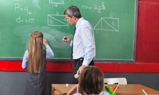 Rear,Of,Little,Girl,Solving,Mathematics,On,Board,With,Teacher